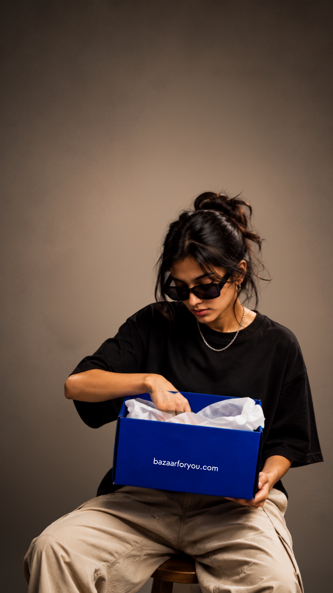 Woman in black opening a blue BazaarForYou box against a brown studio backdrop